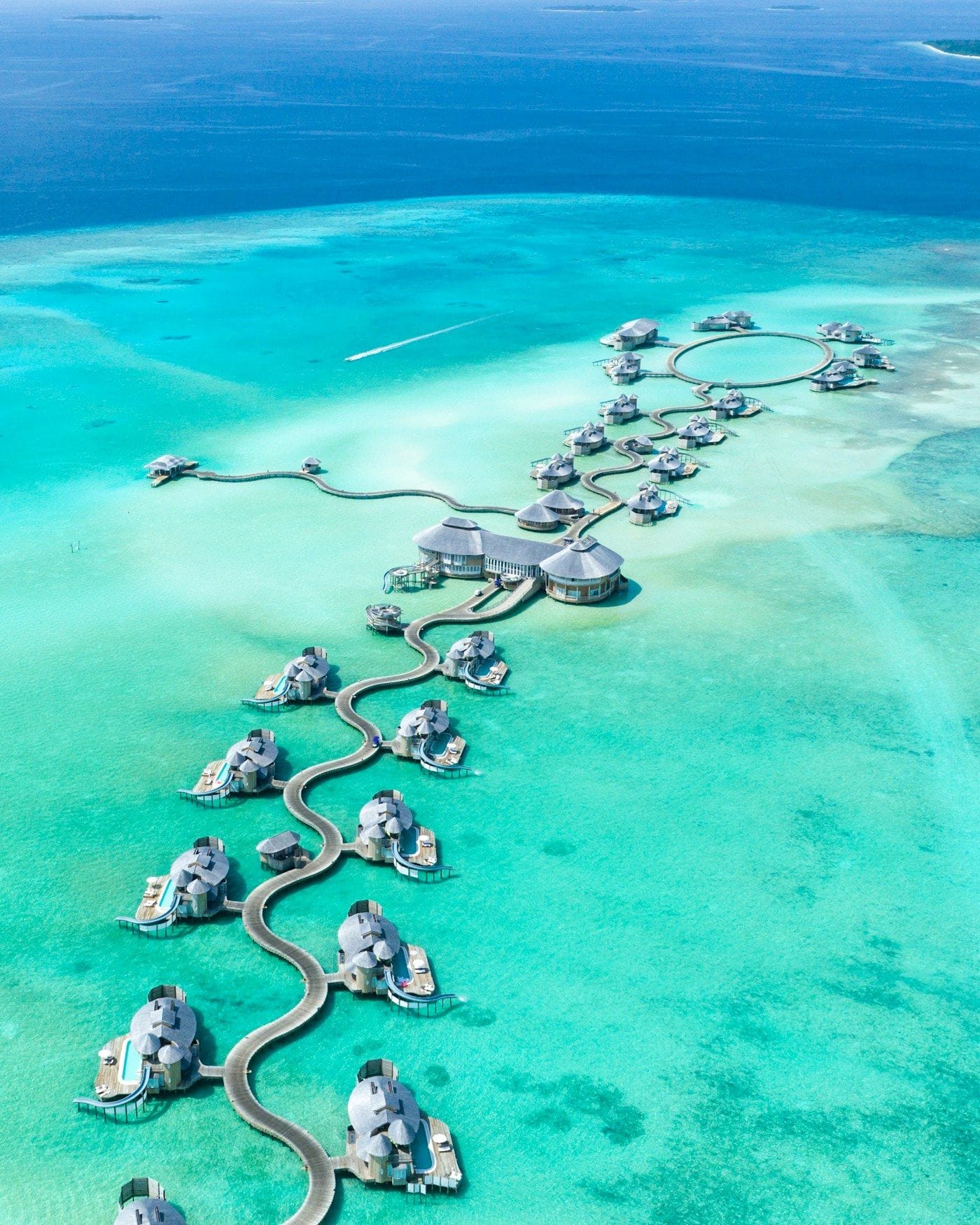 Overwater villas curving across a shallow turquoise Maldivian lagoon